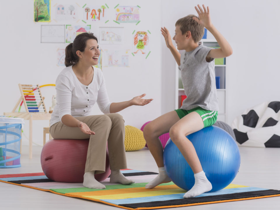 Blonder Junge und dunkelhaarige Frau sitzen auf Gymnastikbällen im Übungsraum